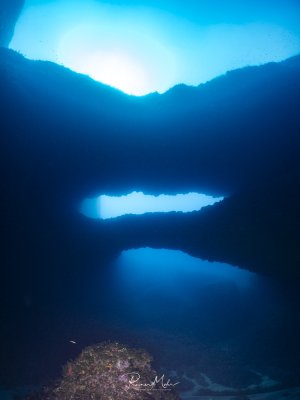der Double Arch in Gozo in der Xwejni Bay im Gegenlicht. Die Sonne scheint dramatisch von oben durch die Torbögen